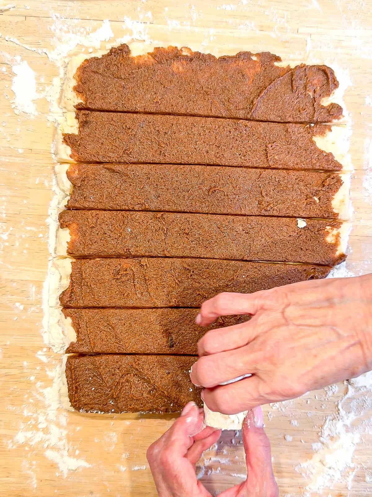 Rolling up strips of dough into a cinnamon roll.