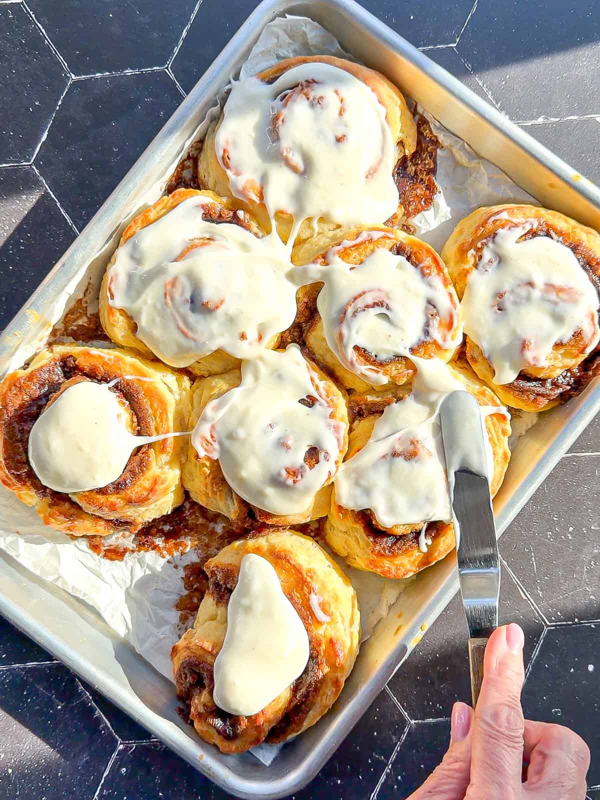 Spreading frosting on cinnamon roll biscuits.
