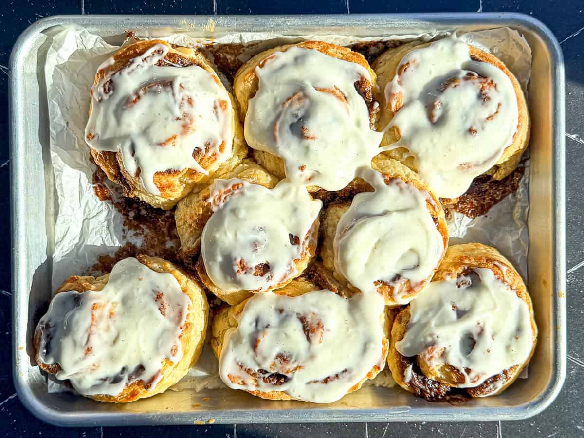 Frosted cinnamon rolls on a parchment paper lined sheet pan.