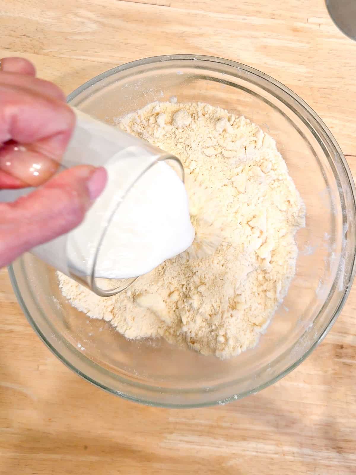 Adding buttermilk to flour and butter mixture to make biscuit dough.