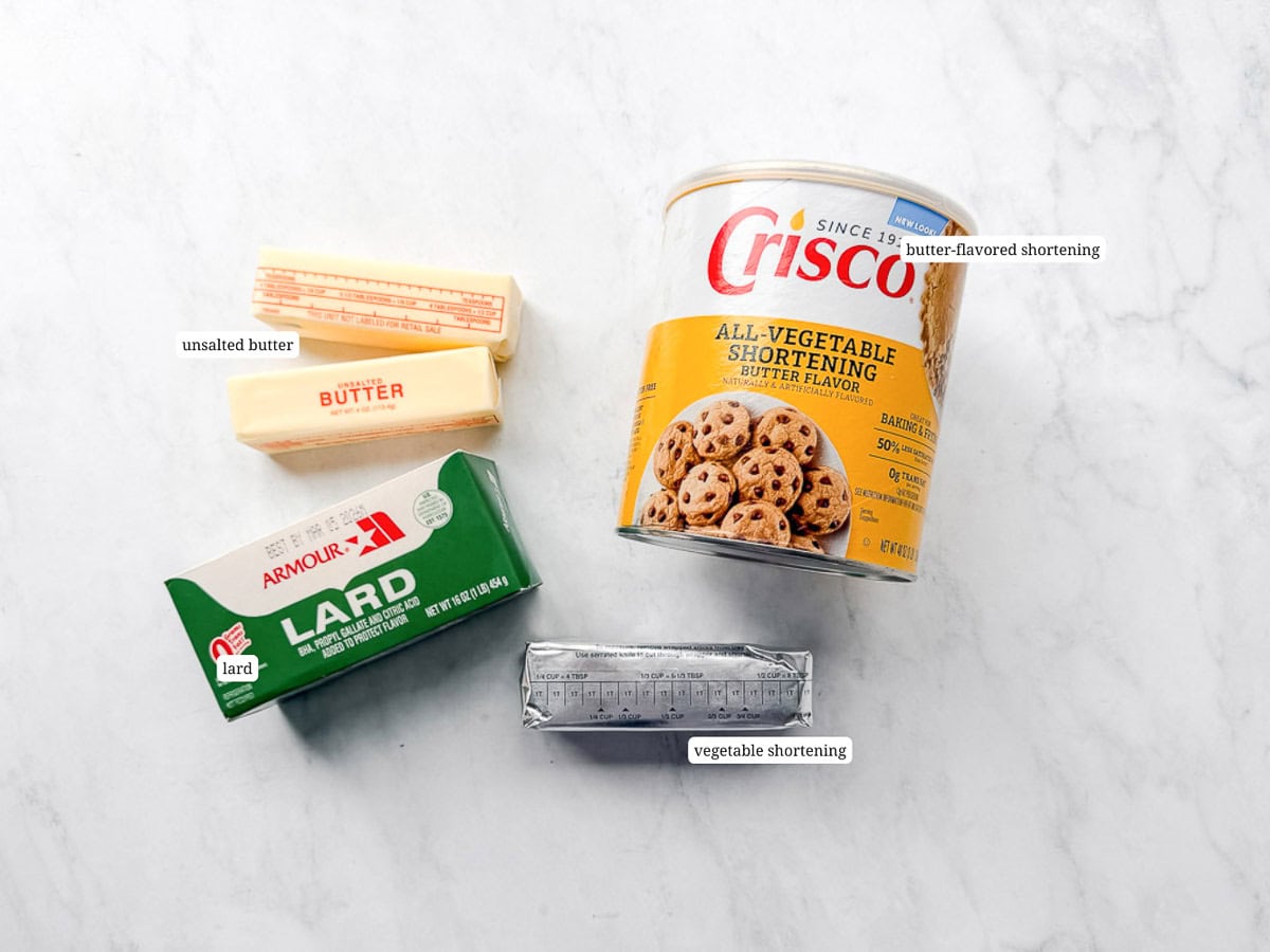 Unsalted butter, lard, butter flavored shortening, and vegetable shortening on a white counter.