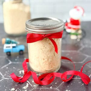 A mason jar filled with biscuit mix with a ribbon tied around it and ribbon on the counter.