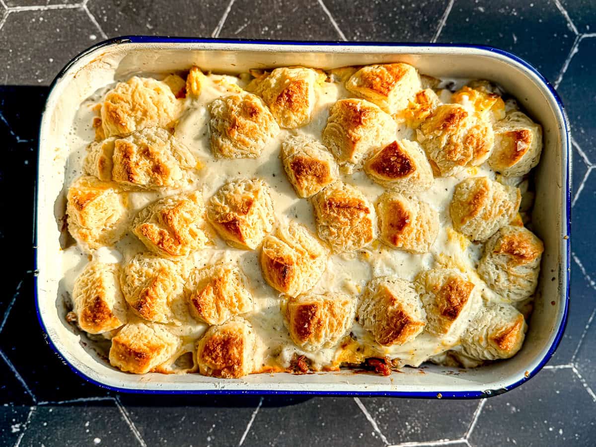 Biscuits and gravy casserole in a white casserole dish on a black background.