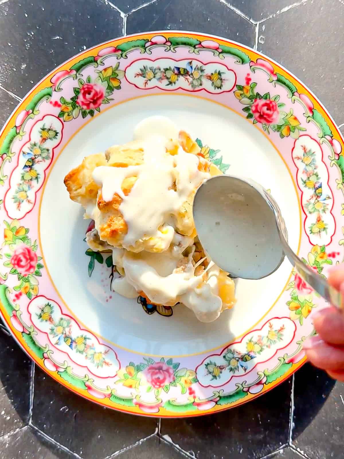 Spooning gravy over a casserole on a floral plate.