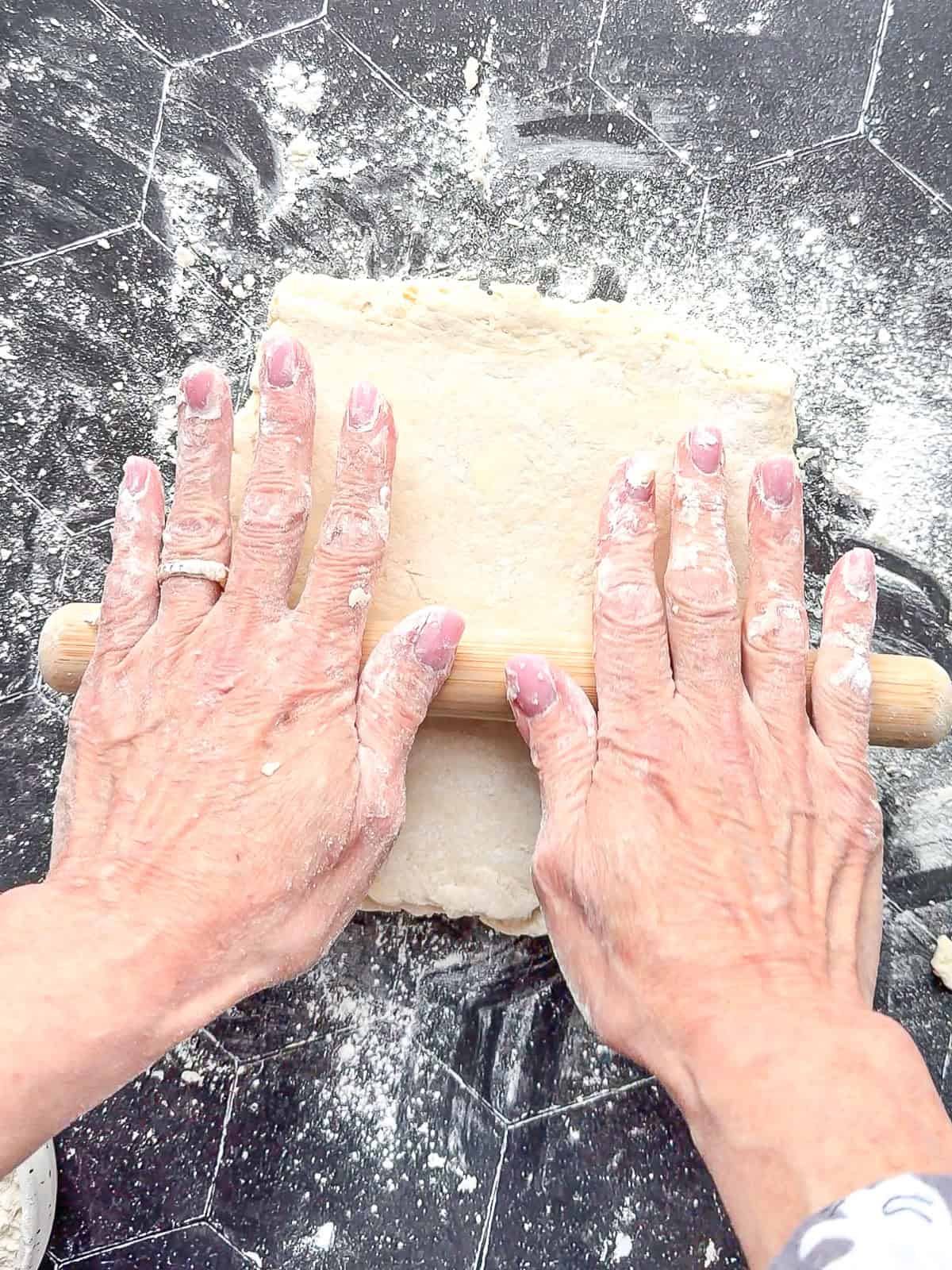Rolling out biscuit dough on a black counter.