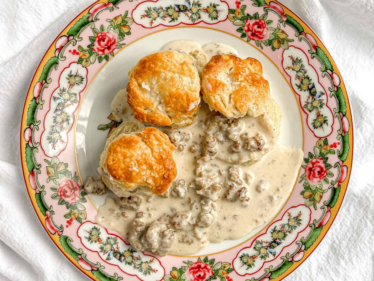Biscuits and sausage gravy on a floral plate.