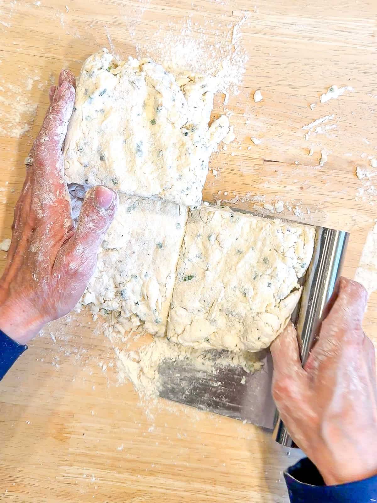 Using a bench scraper to stack squares of biscuit dough on top of one another.