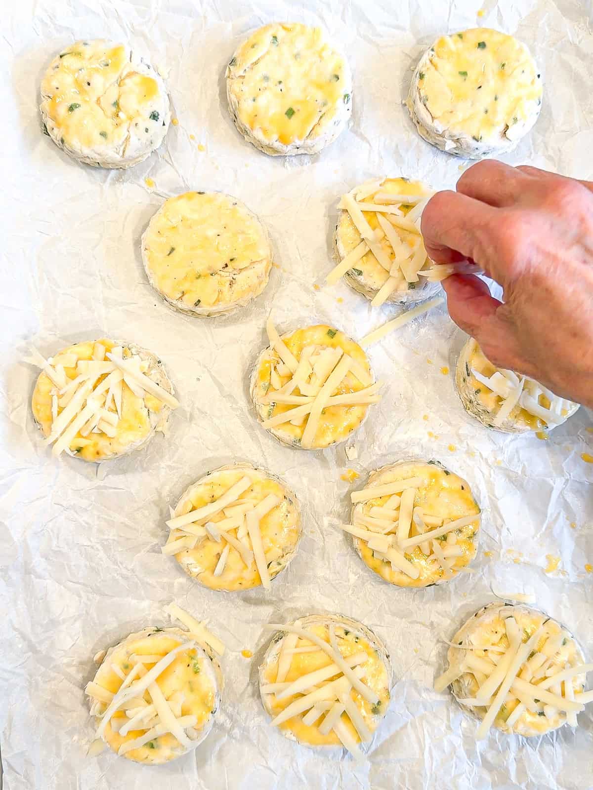 Topping unbaked biscuits with shredded Gruyere cheese.