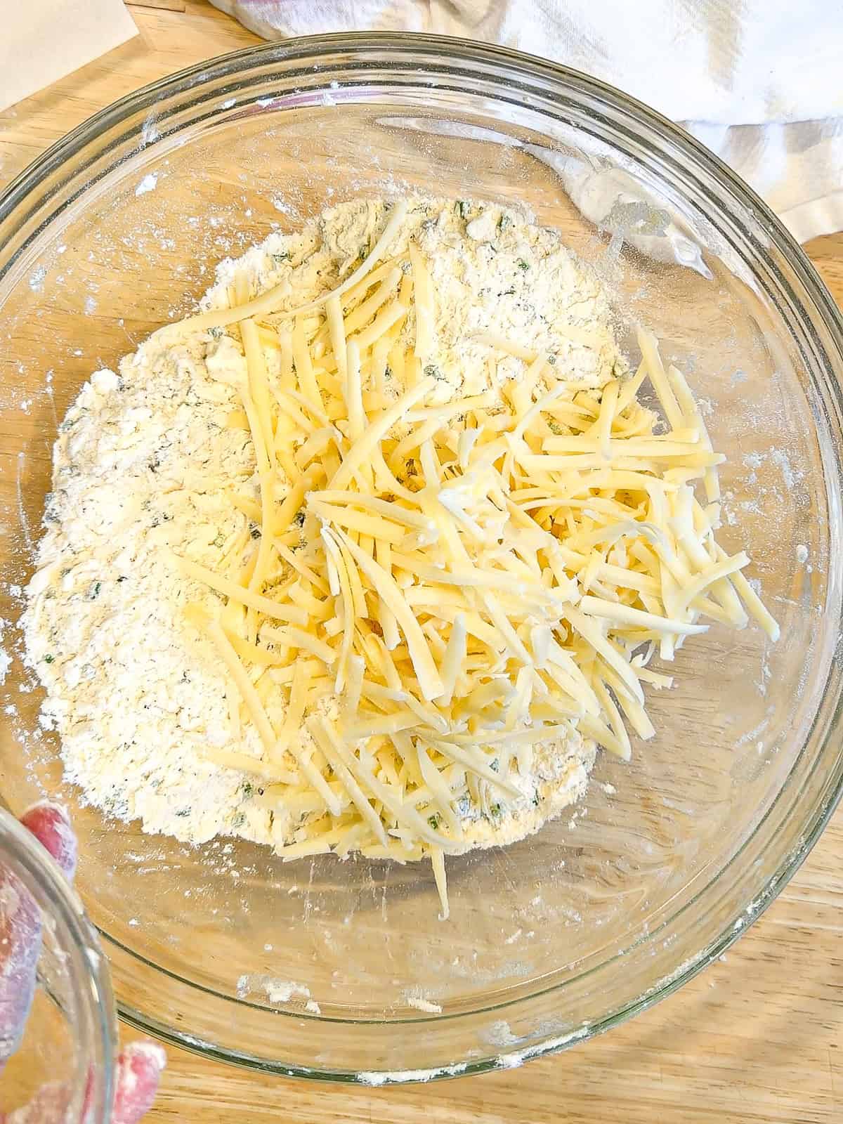 Adding shredded Gruyere cheese to dry ingredients to make biscuits.