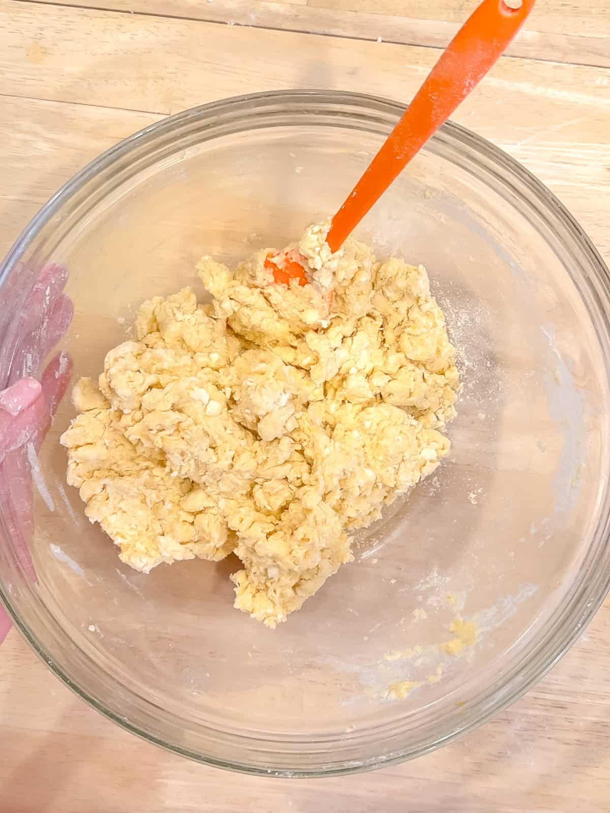 Scone dough in a glass bowl with an orange spatula.