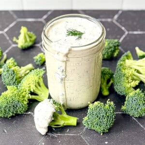 Ranch dressing in a mason jar on a black background with broccoli florets.