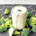 Ranch dressing in a mason jar on a black background with broccoli florets.