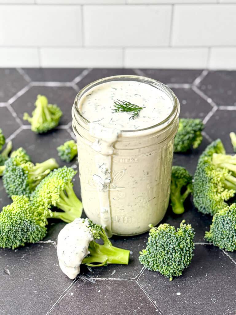 Ranch dressing in a mason jar on a black background with broccoli florets.