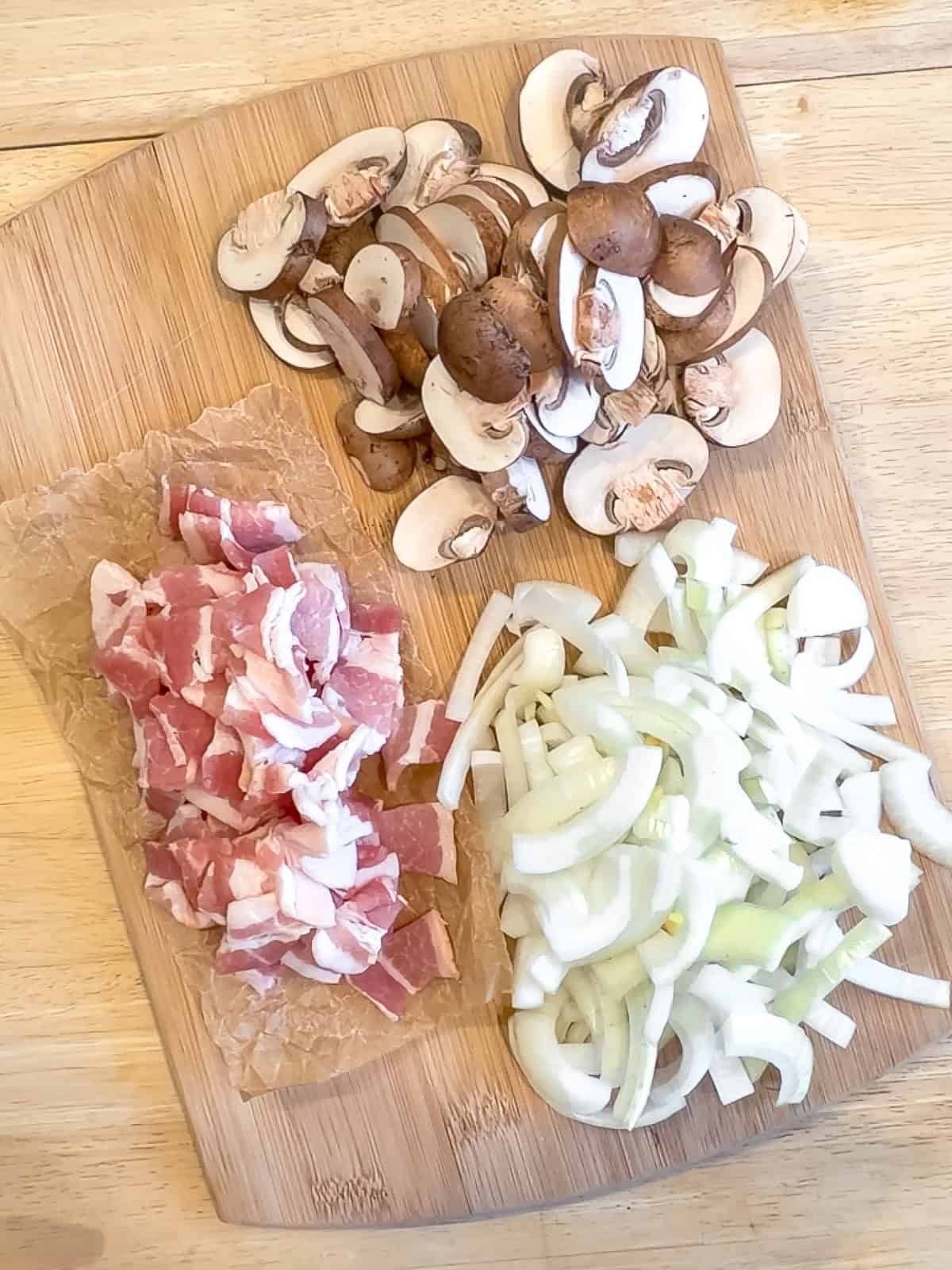 Chopped bacon, onions, and mushrooms on a cutting board.