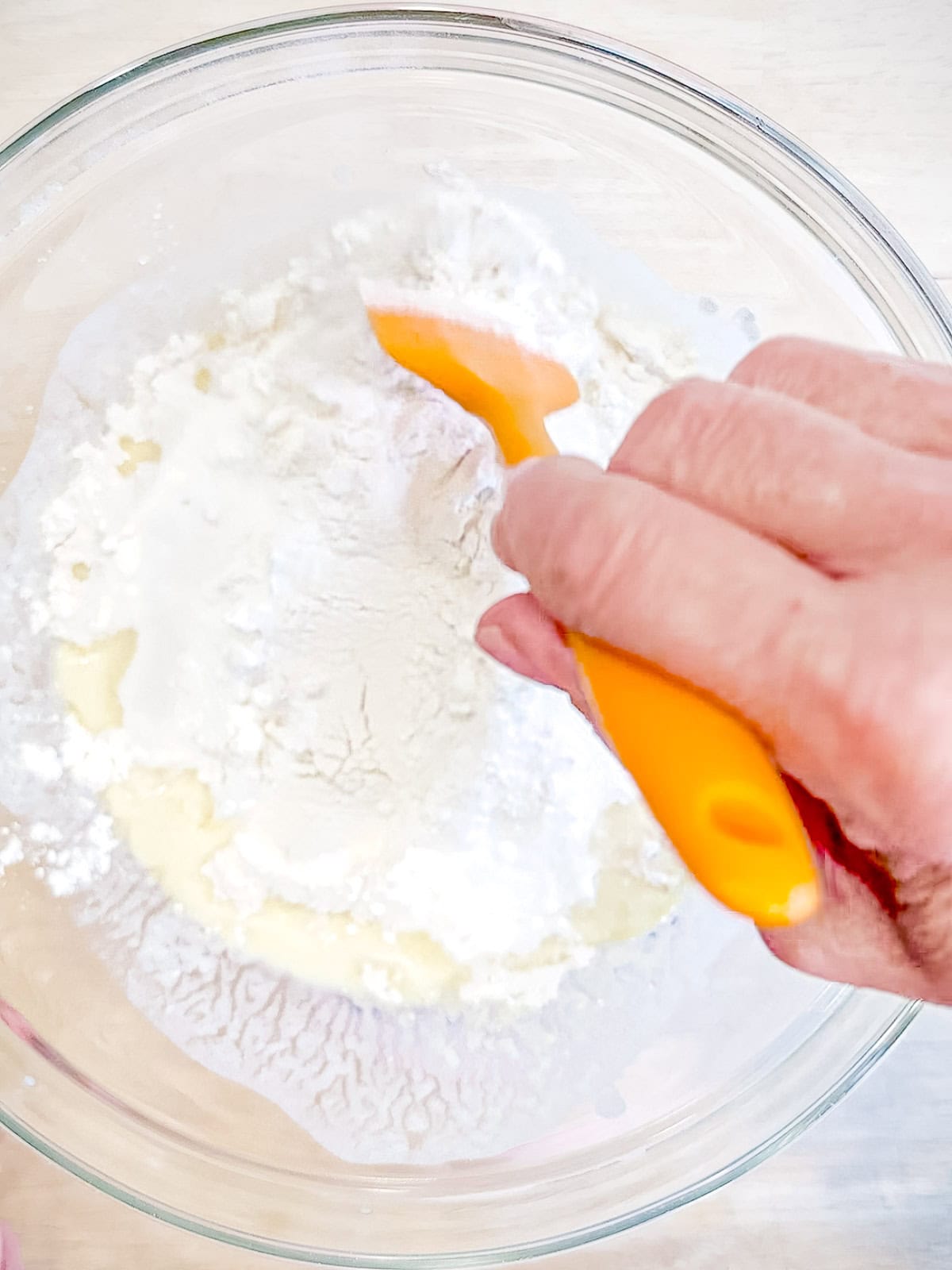 Mixing waffle batter in a glass bowl using an orange spatula.