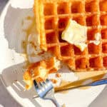 Buttermilk waffles with butter and syrup on a white plate.