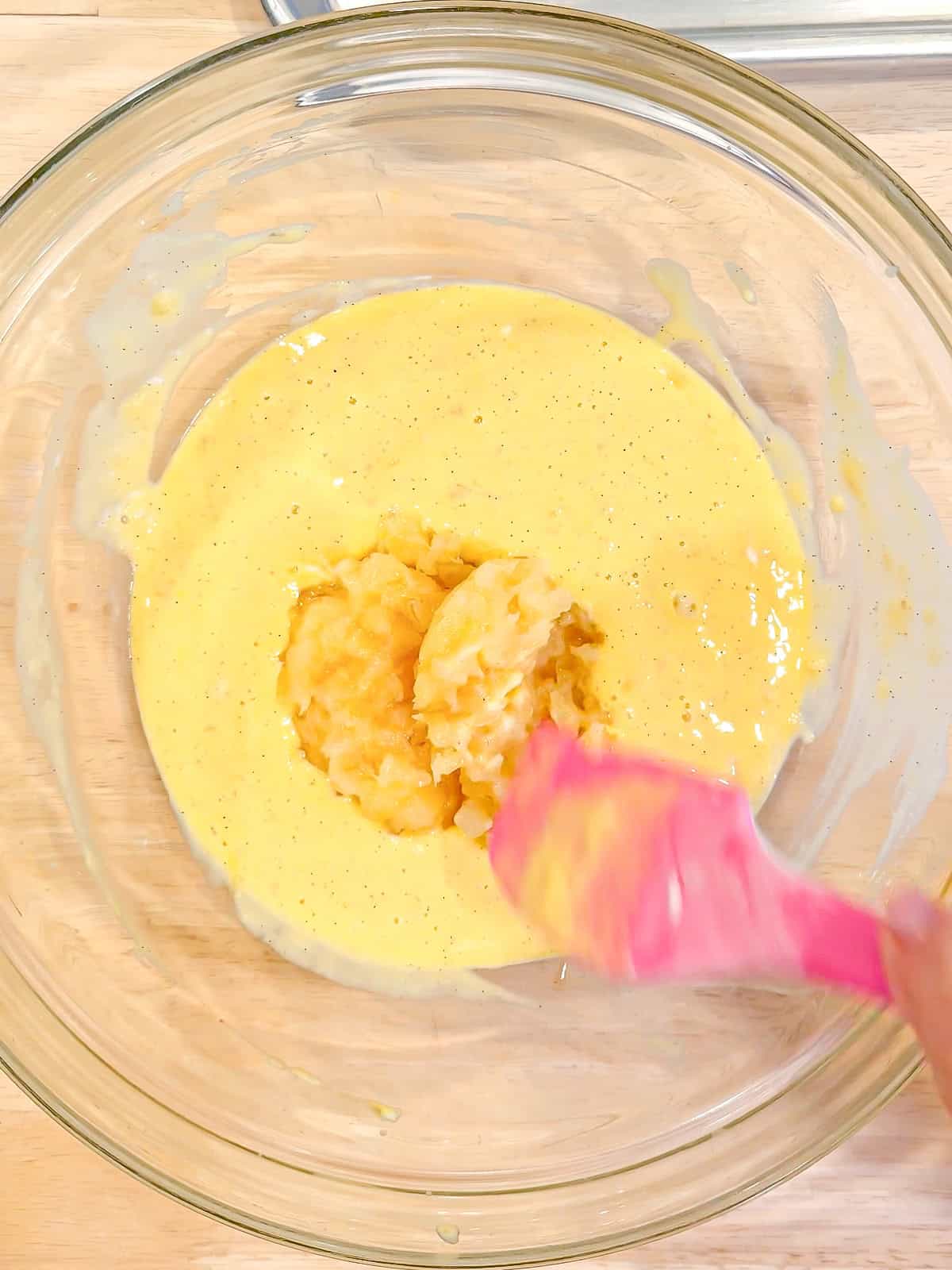 Adding crushed pineapple to wet ingredients in a glass bowl.
