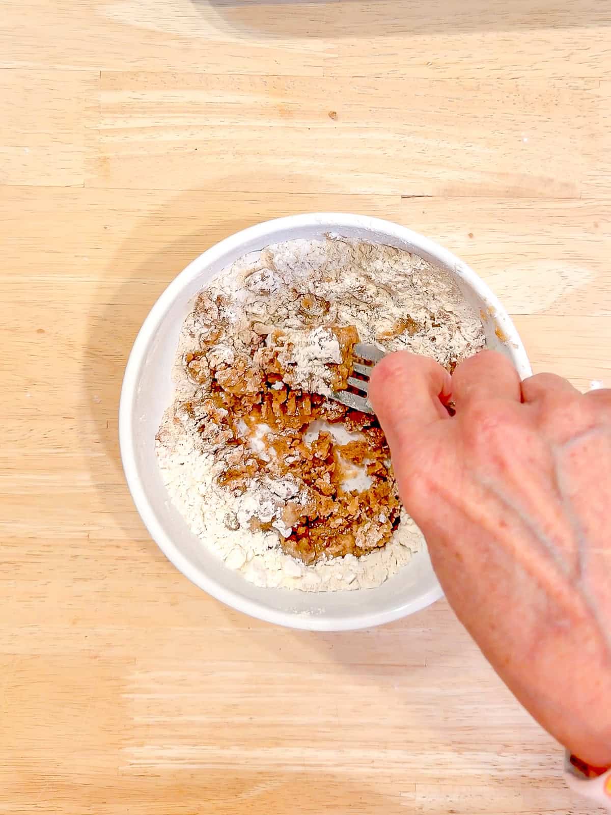 Using a fork to make streusel in a white ceramic bowl.