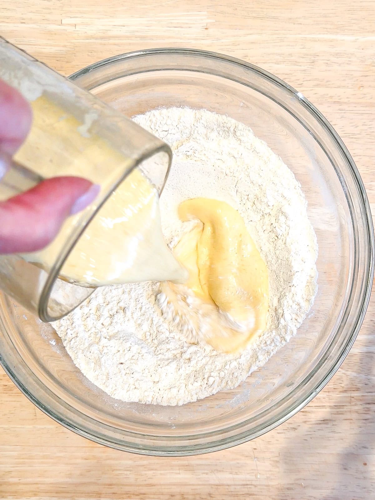 Adding wet ingredients to dry ingredients in a glass bowl.
