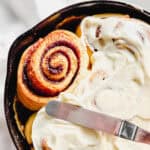 Spreading frosting on cinnamon rolls in a cast-iron pan.
