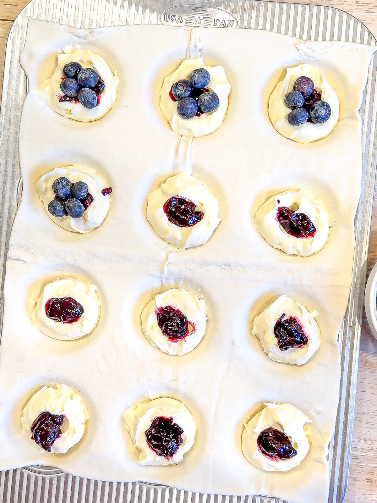 Adding jam and blueberries to the top of cheesecake filling on puff pastry.
