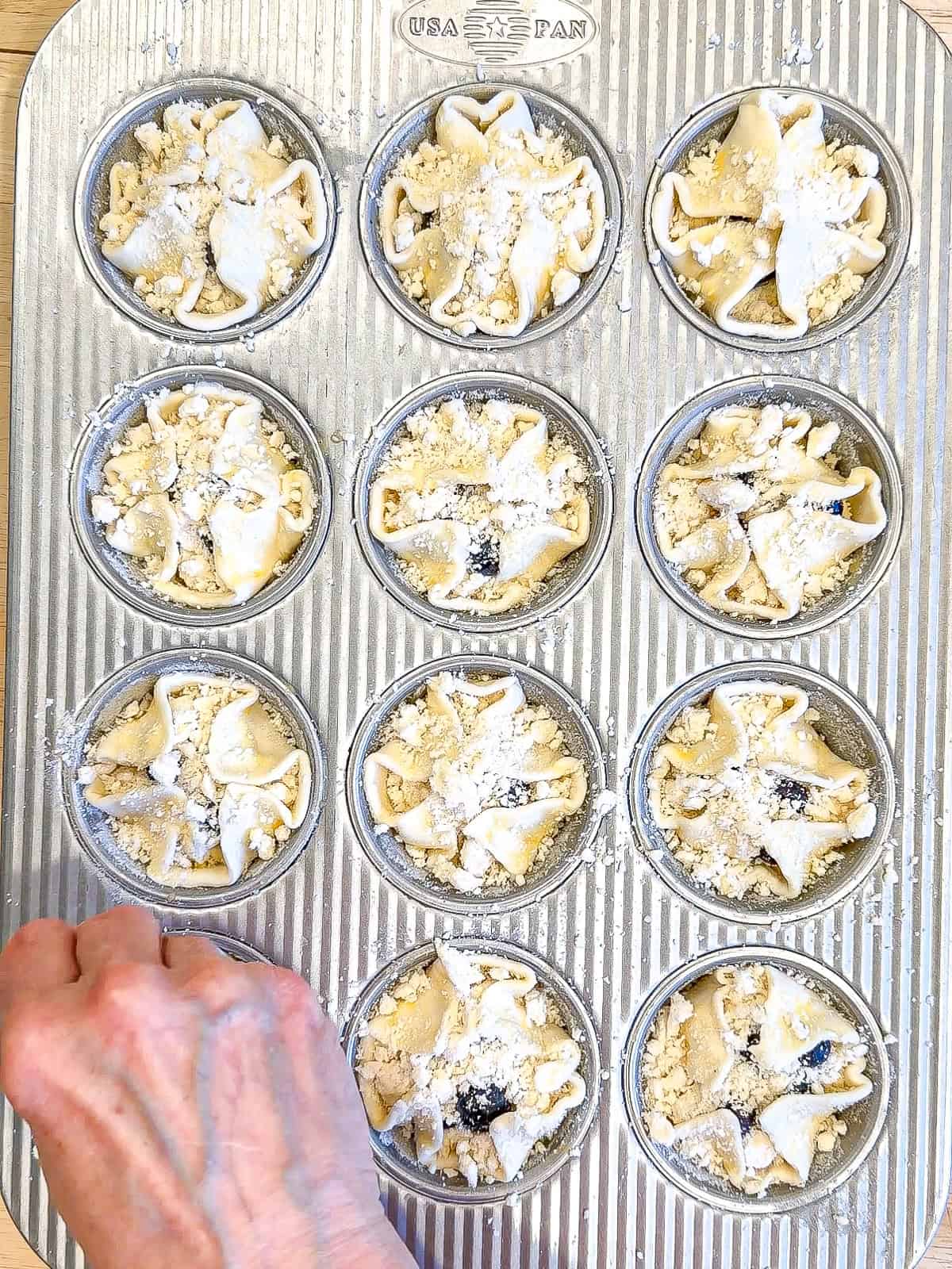 Sprinkling streusel on muffins and a muffin pan.