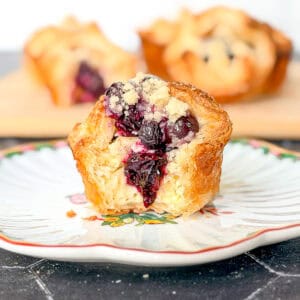 A blueberry caramelized cheesecake croissant on a white and flowered plate.
