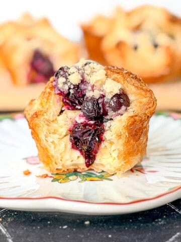 A blueberry caramelized cheesecake croissant on a white and flowered plate.