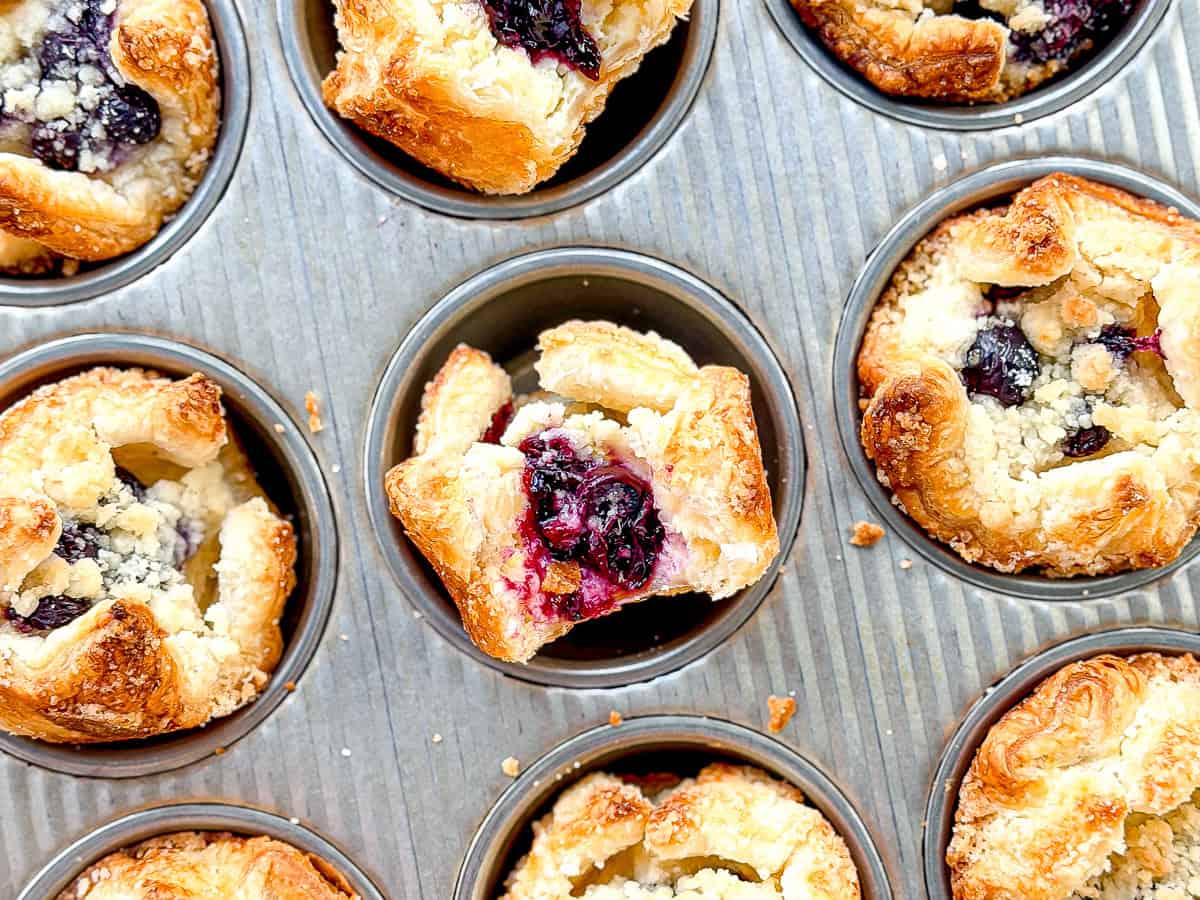 Blueberry caramelized cheesecake croissants in a muffin pan.