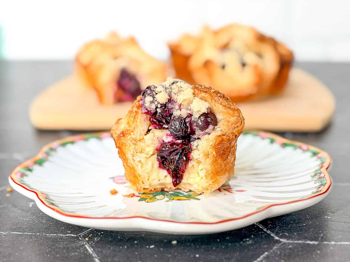 A blueberry caramelized cheesecake croissant on a white and flowered plate.