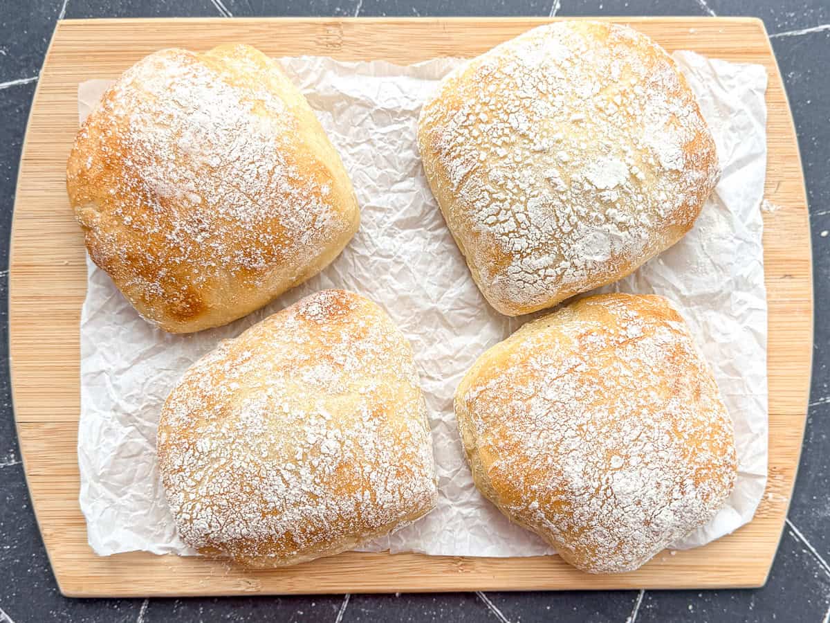 Ciabatta rolls on a parchment paper covered wooden cutting board.