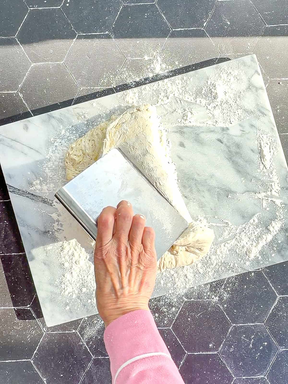 Using a bench scraper to fold ciabatta dough over onto itself.