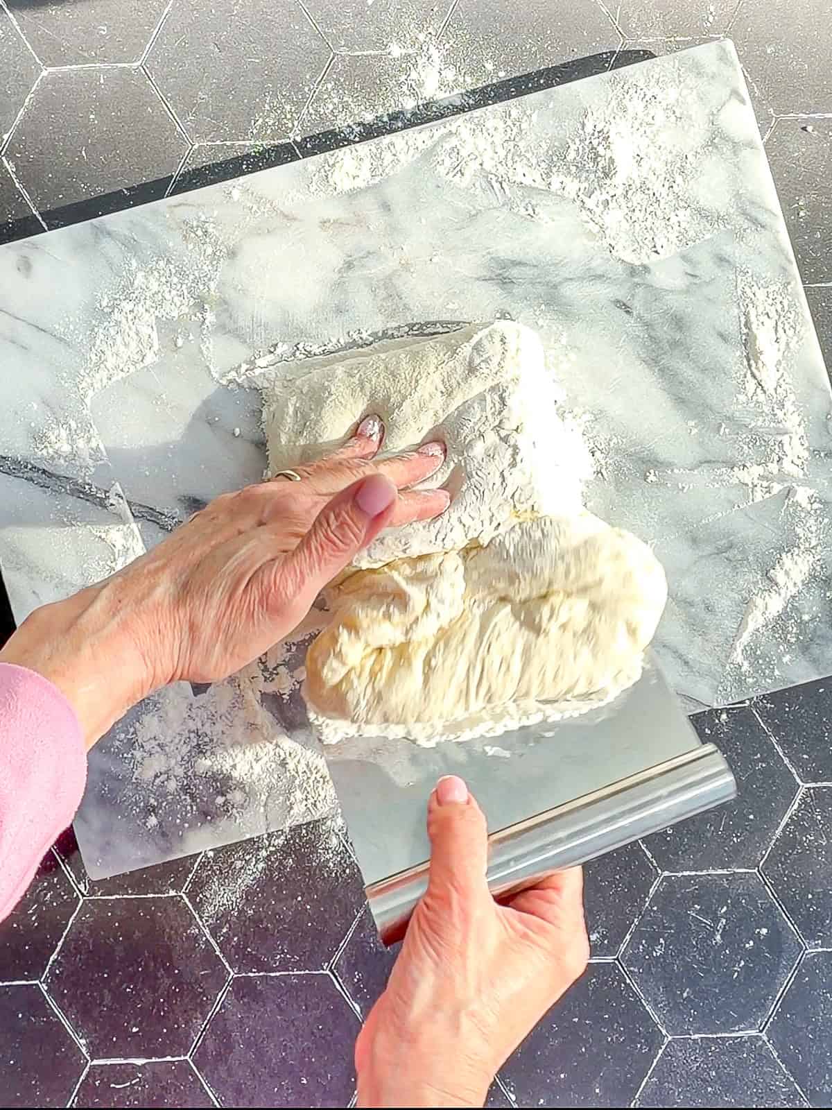 Using a bench scraper to fold ciabatta dough over onto itself.