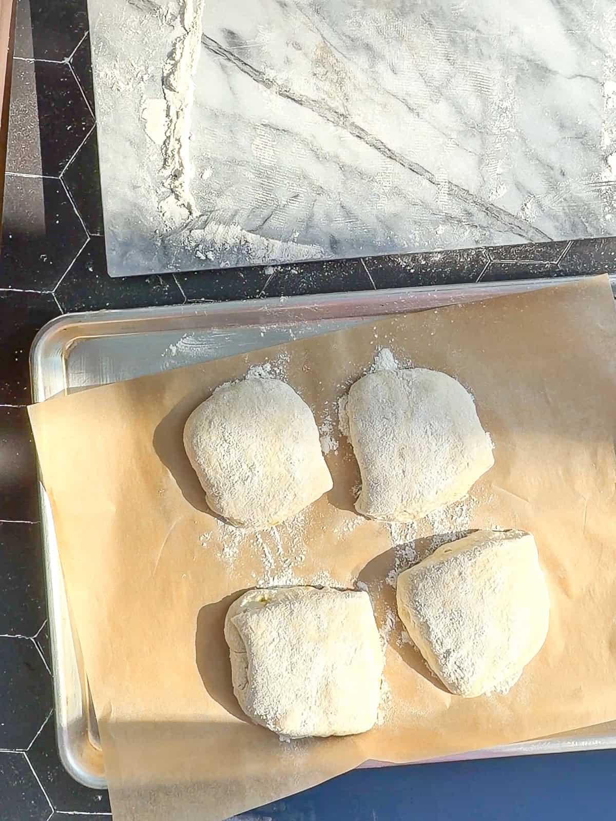 Unbaked ciabatta rolls transferred onto a parchment paper lined sheet pan.
