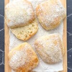 Ciabatta rolls on a parchment paper covered wooden cutting board.