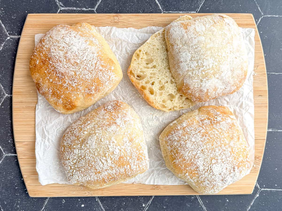 Ciabatta rolls on a parchment paper covered wooden cutting board.