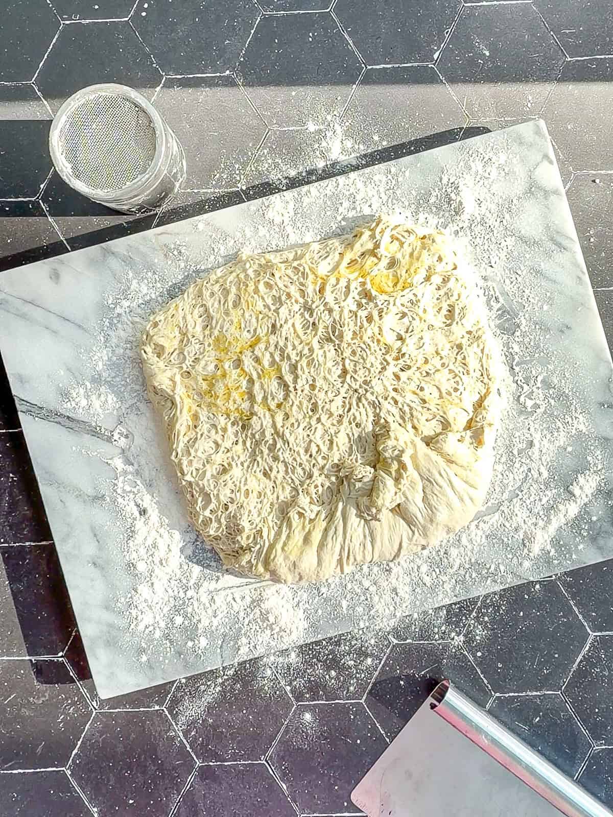 Fermented ciabatta dough on a marble works surface.