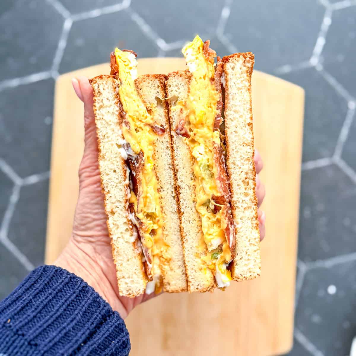 Hand holding a breakfast sandwich with a slice of sheet pan Denver omelette in the middle.