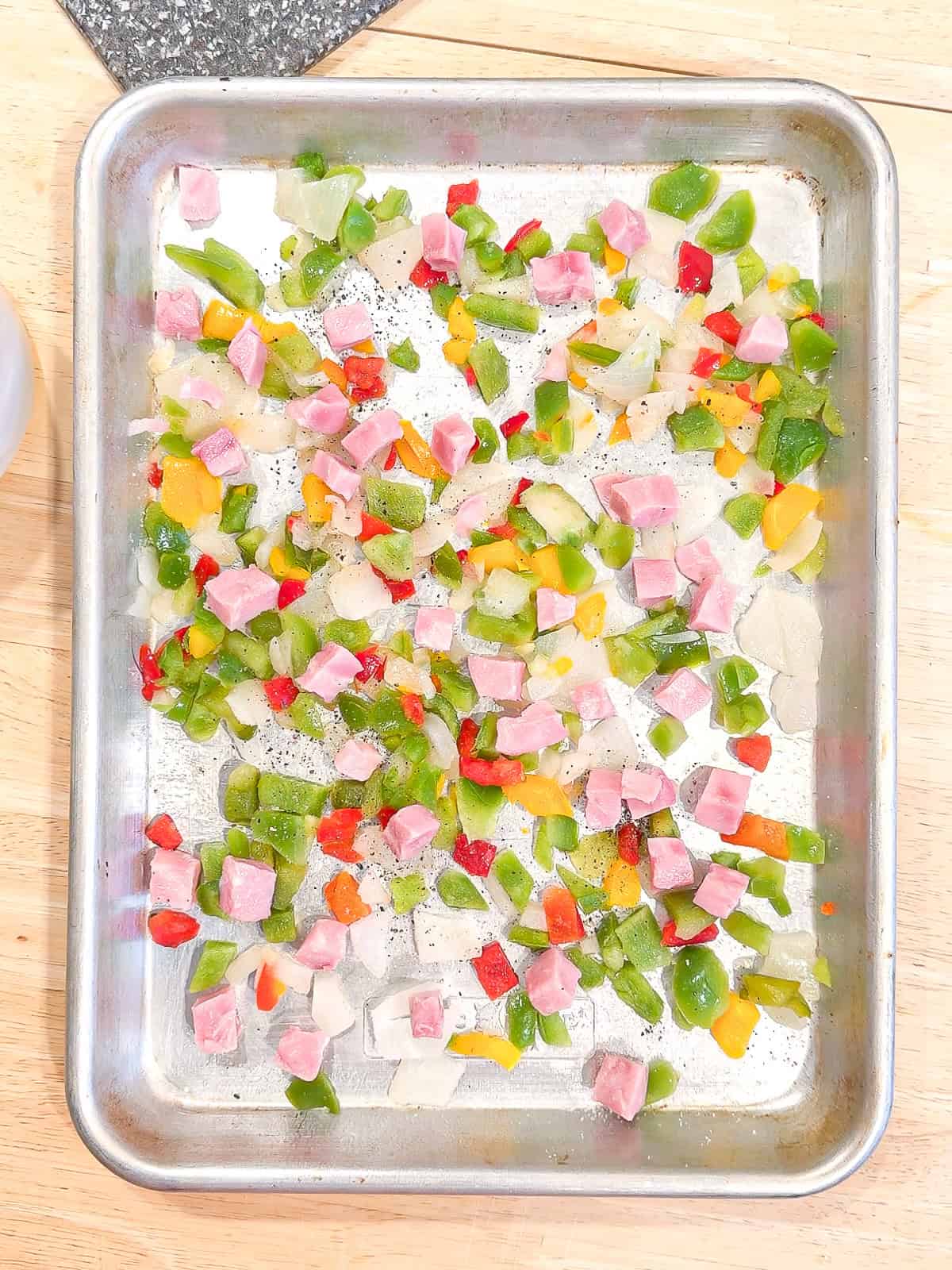 Frozen bell peppers, onions, and diced ham on a small sheet pan.