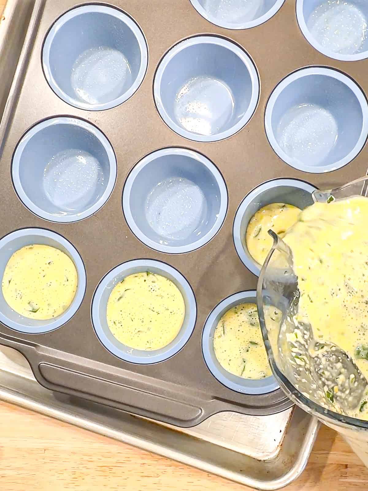 Pouring blended egg mixture into a muffin pan.