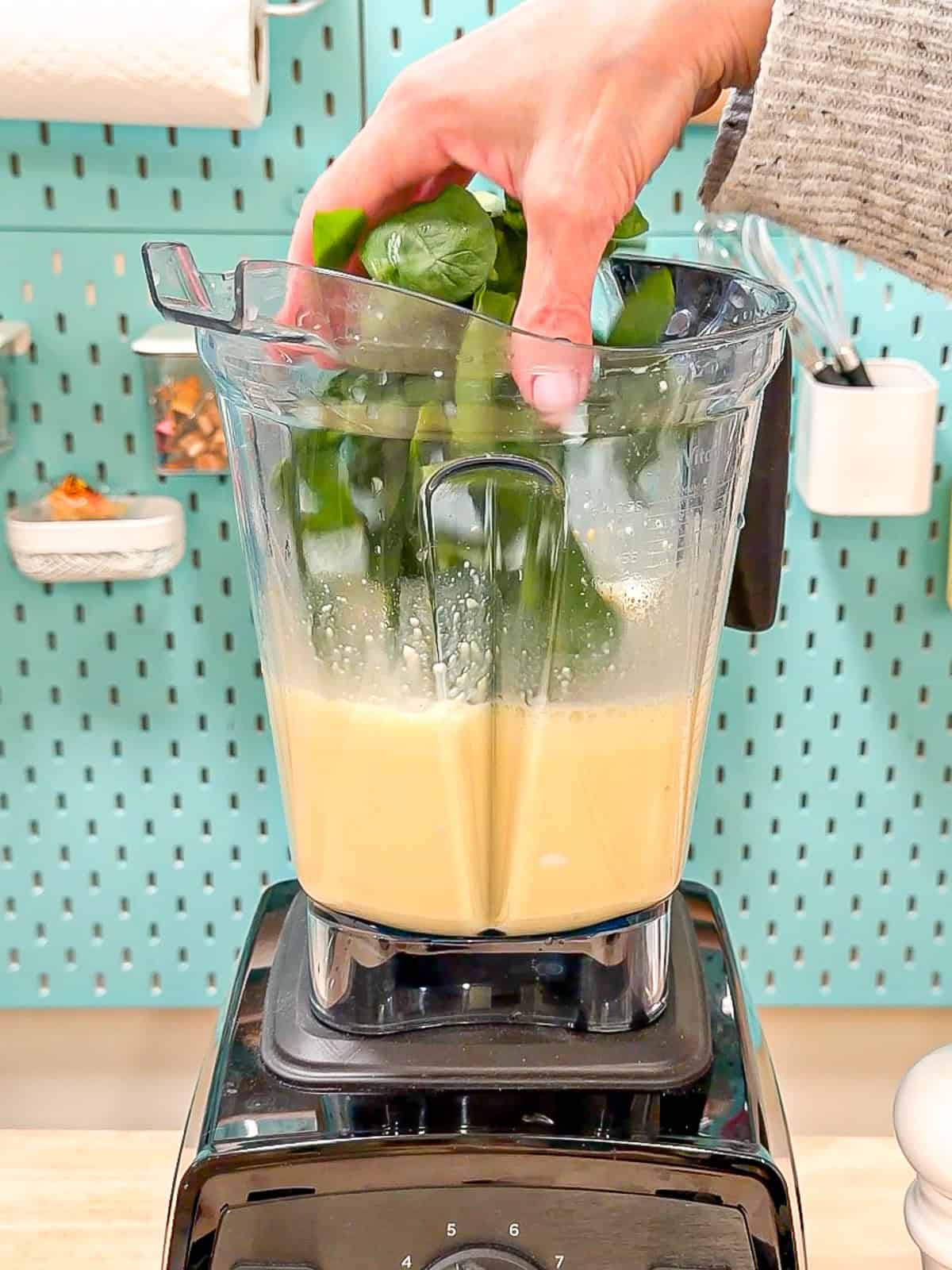 Adding spinach to blended eggs in a blender.