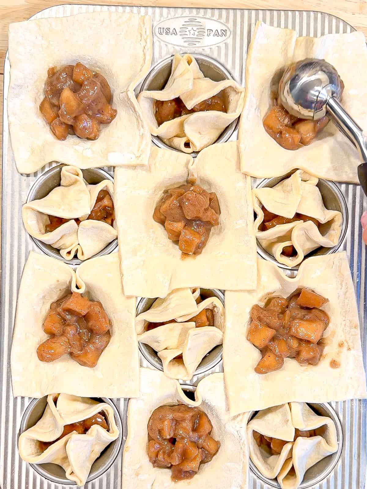 Scooping apple filling into puff pastry squares.
