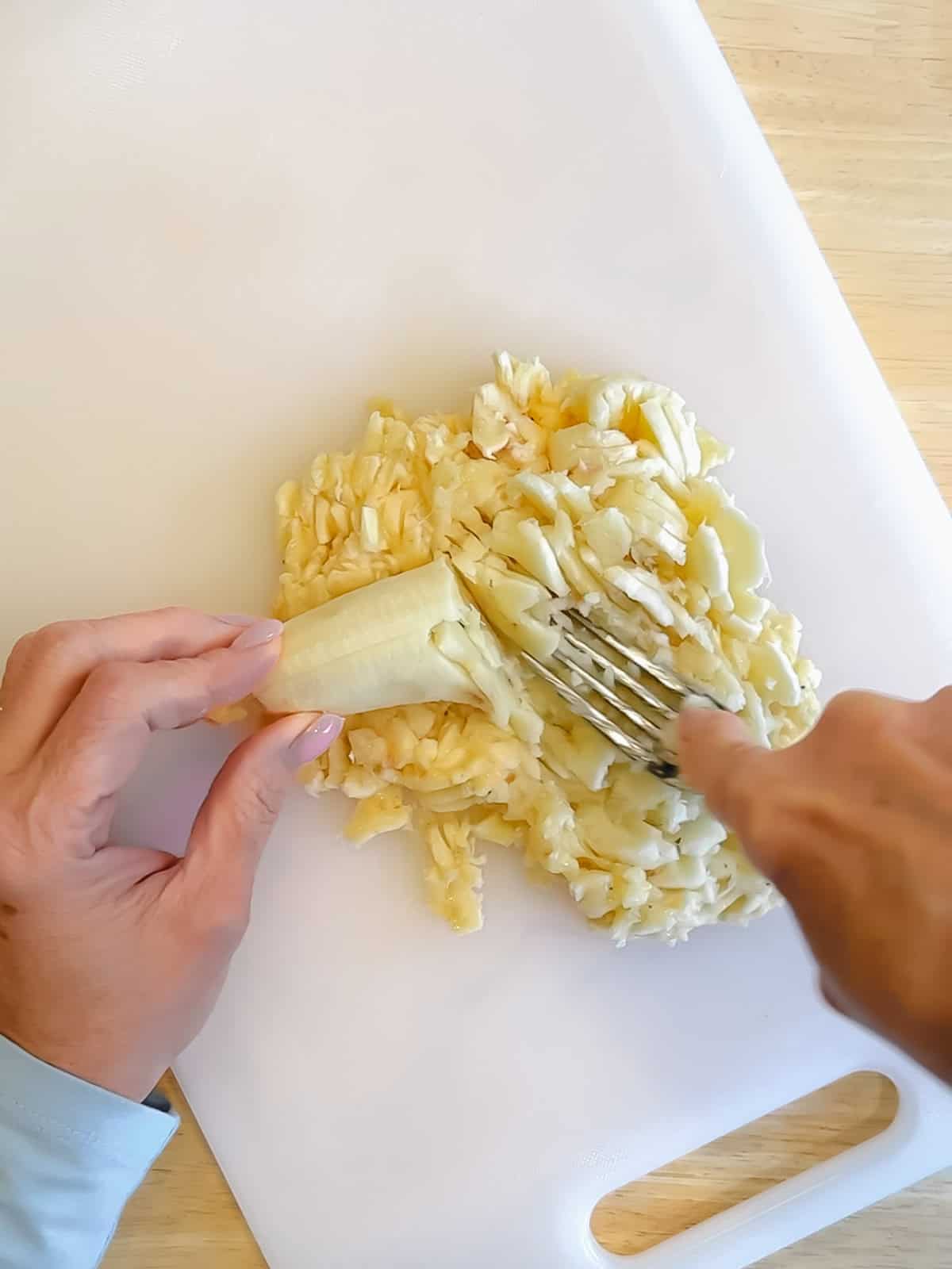 Using a fork to mash a banana on a cutting board.