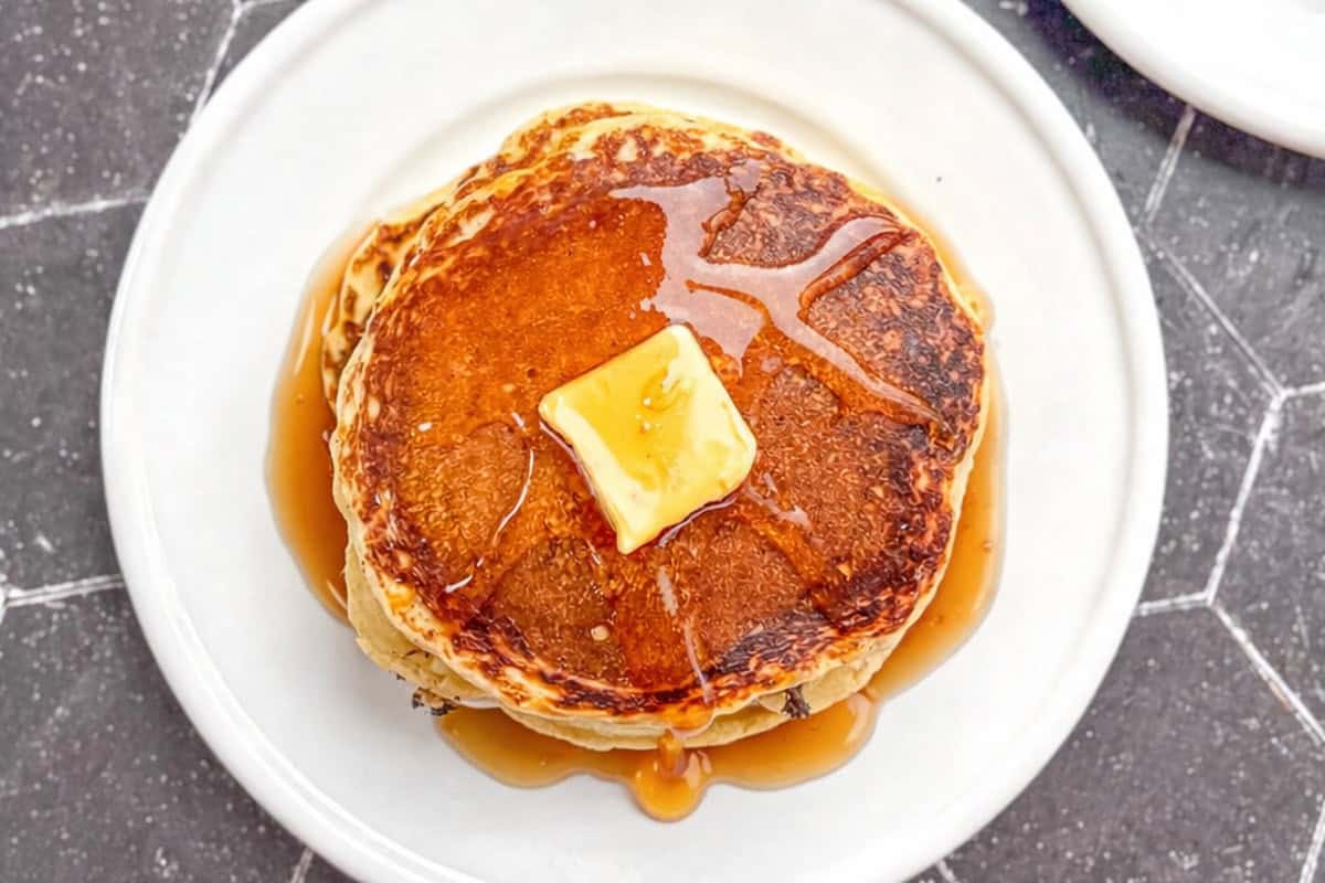 Pancakes with butter and maple syrup on a white plate.