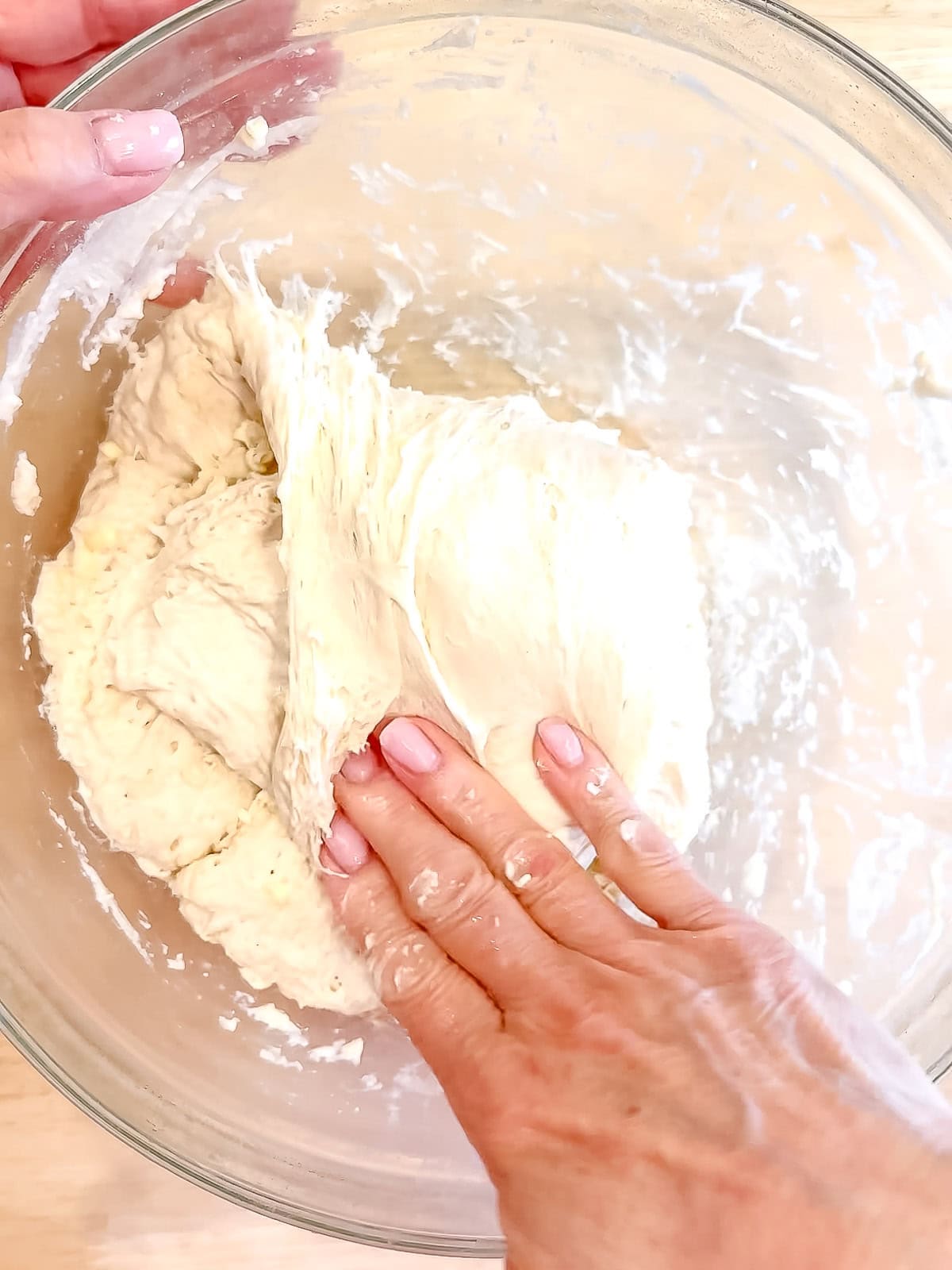 Folding one side of dough over the rest of the dough in a glass bowl.