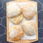 Ciabatta rolls on a parchment paper covered wooden cutting board.