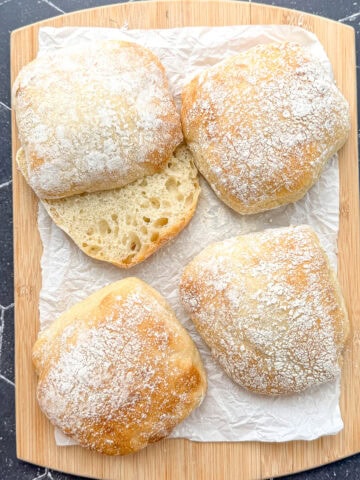 Ciabatta rolls on a parchment paper covered wooden cutting board.