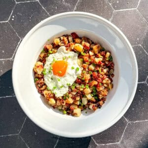 A white bowl containing corned beef hash and a fried egg with chopped chives on top.