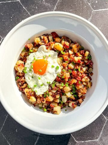 A white bowl containing corned beef hash and a fried egg with chopped chives on top.