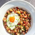 A white bowl containing corned beef hash and a fried egg with chopped chives on top.